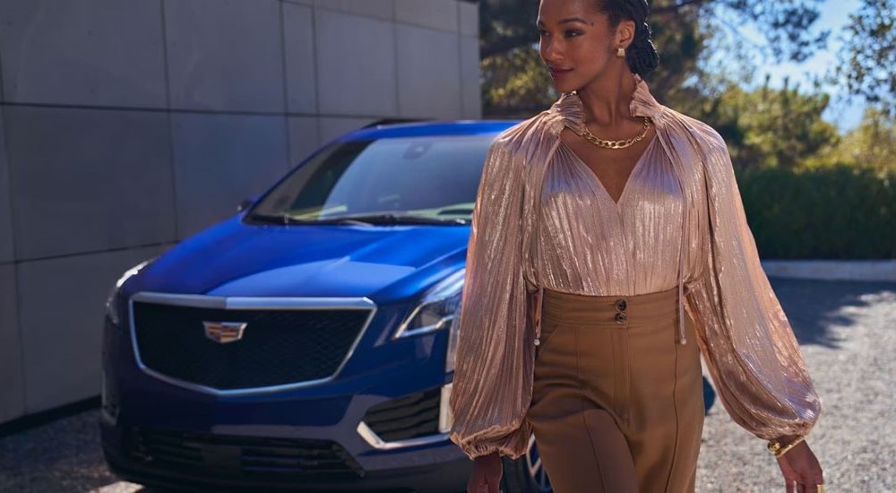 A woman is walking past a parked blue 2024 Cadillac XT5 after leaving a Cadillac dealer near Minneapolis.