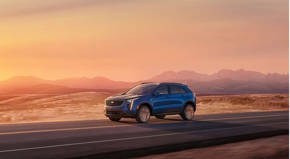 A blue 2023 Cadillac XT4 driving on an open road at sunset after visiting a Cadillac dealer.