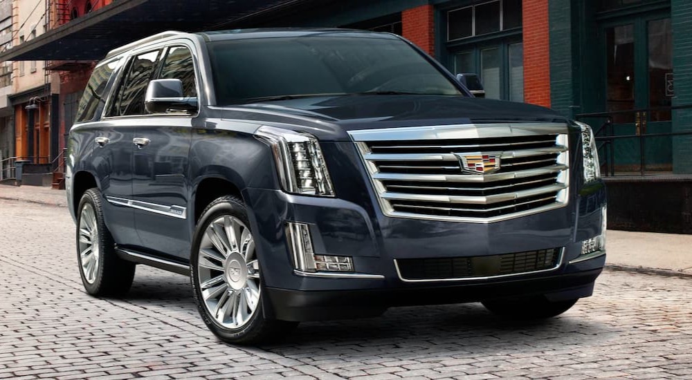 A blue 2020 Cadillac Escalade parked on a cobbled street near a used Cadillac dealership.