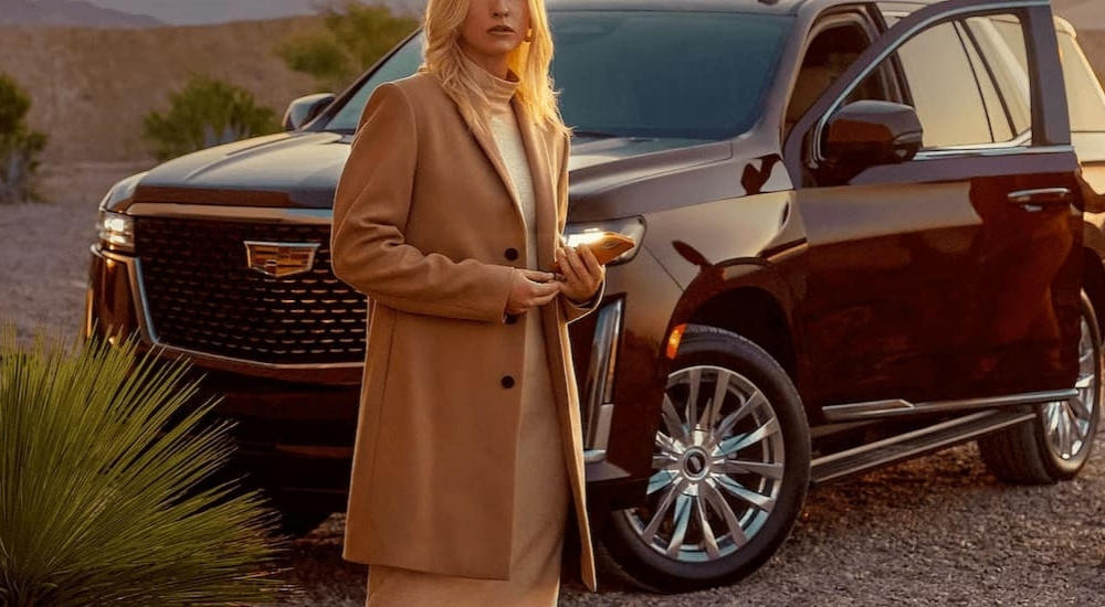 A woman standing near a 2023 used Cadillac Escalade for sale in a desert.