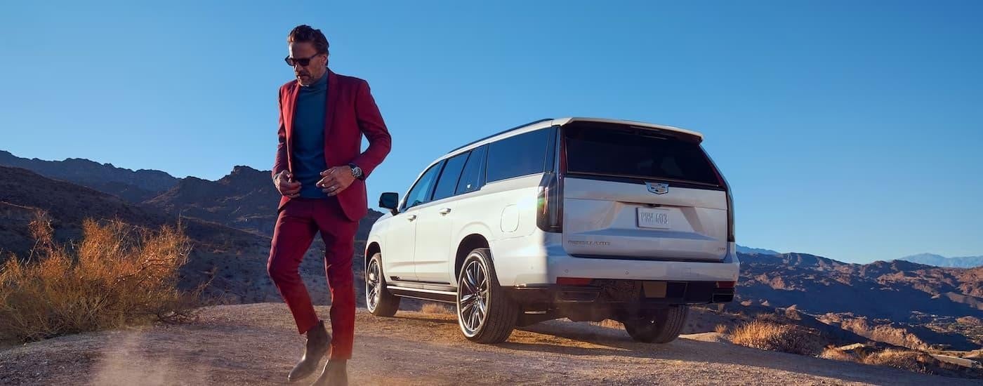 A man is shown walking away from a white 2023 Cadillac Escalade parked in a desert.