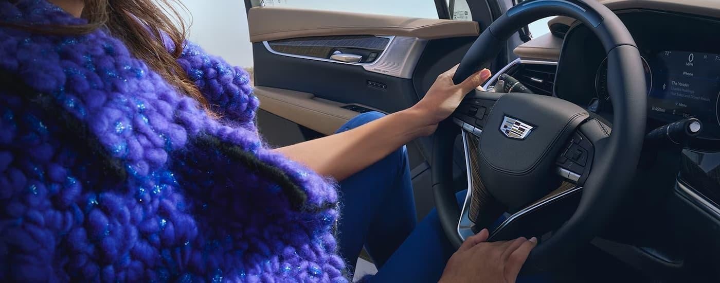 A woman is sitting in the front drivers seat in a 2024 Cadillac XT6 and holding the steering wheel.