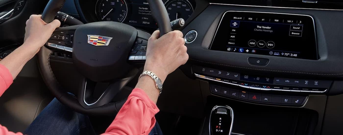 A person is shown holding the steering wheel in a 2023 Cadillac XT4 while listening to music.