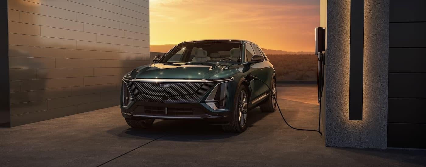 A green 2024 Cadillac LYRIQ is shown charging in a driveway.