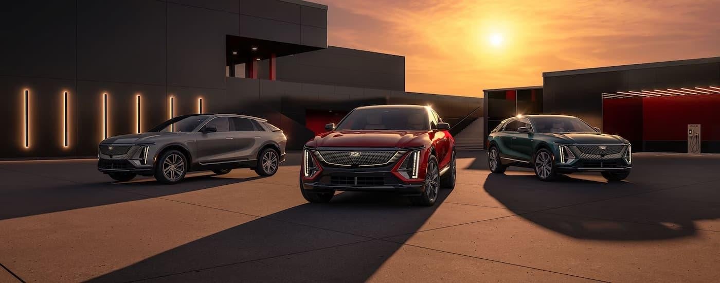 A grey, a red, and a green 2024 Cadillac LYRIQ parked in a driveway during a sunset.