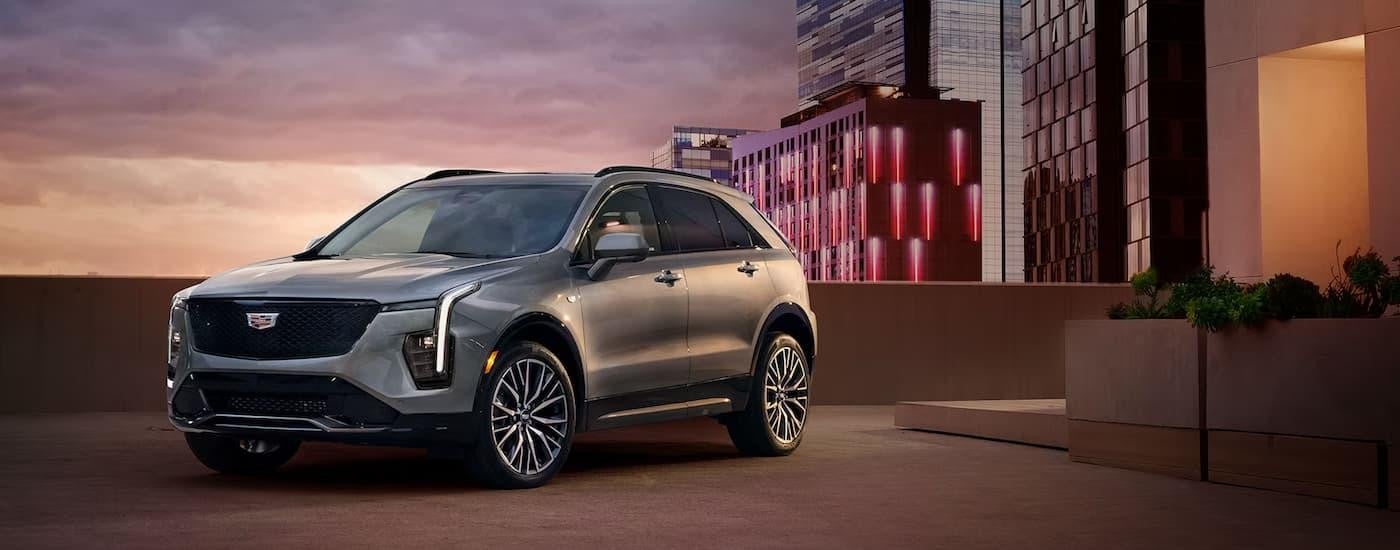 A silver 2024 Cadillac XT4 is parked in a city during a sunset.