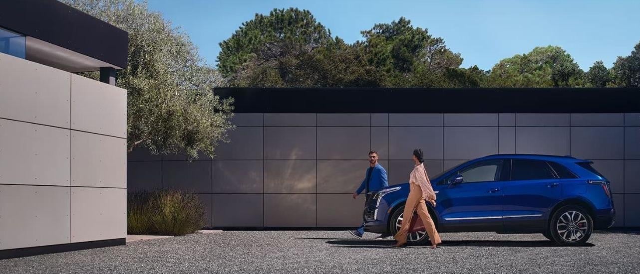 A blue 2024 Cadillac XT5 for sale is shown from the side near a concrete wall.