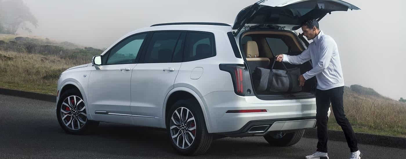 A man is shown putting luggage into the back of a white 2024 Cadillac XT6 parked on the side of a road on a foggy day.