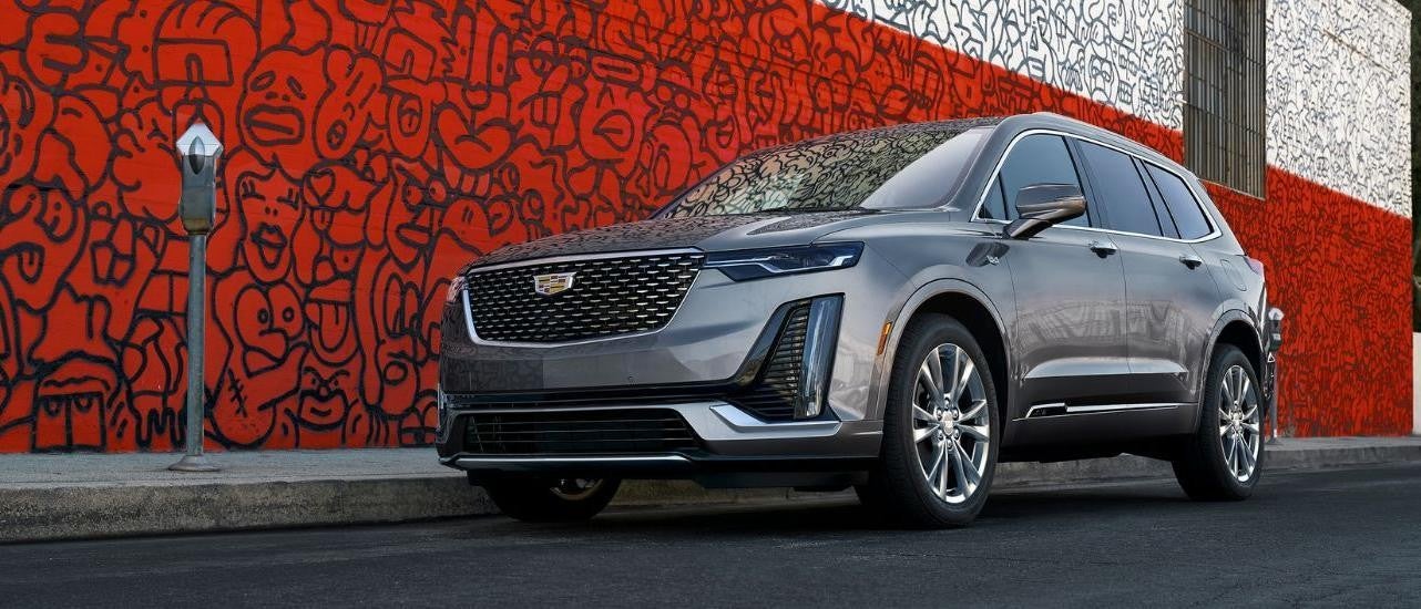 A silver 2021 Cadillac XT6 is shown in front of a wall covered in graffiti.